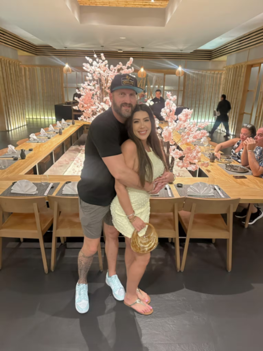 Travis and Chrissy hugging in a restaurant decorated with pink blossoms.
