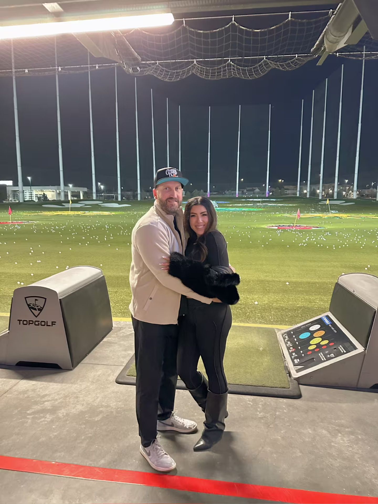 Travis and Chrissy bundled up together at Topgolf at night.