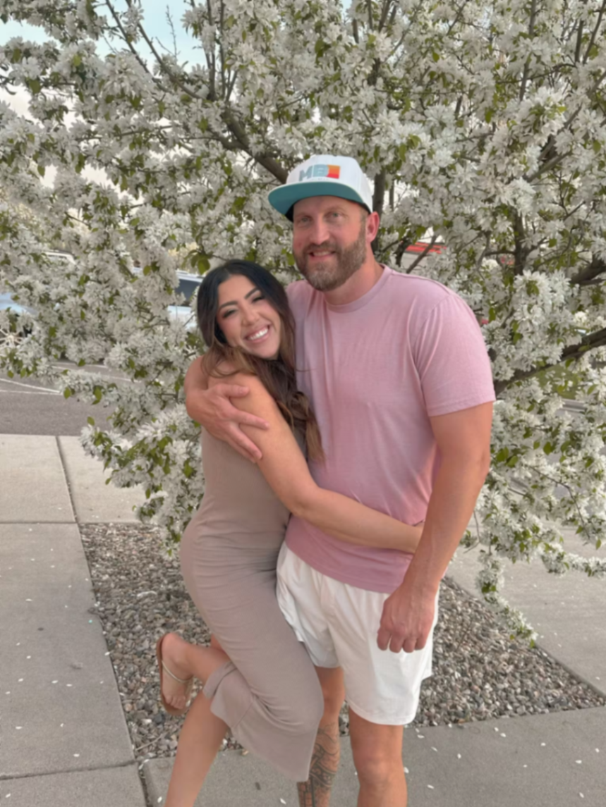 Travis and Chrissy embracing in front of blooming white trees.