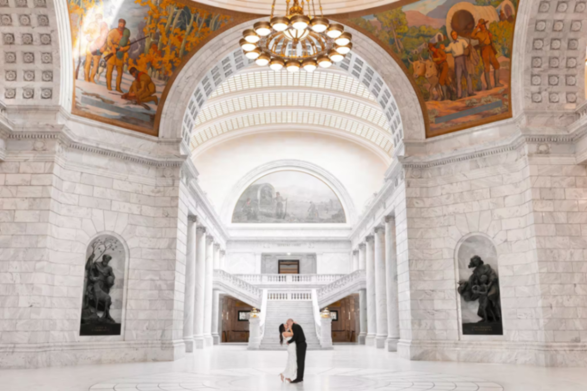 Travis and Chrissy sharing a kiss beneath the grand rotunda of the Utah State Capitol.